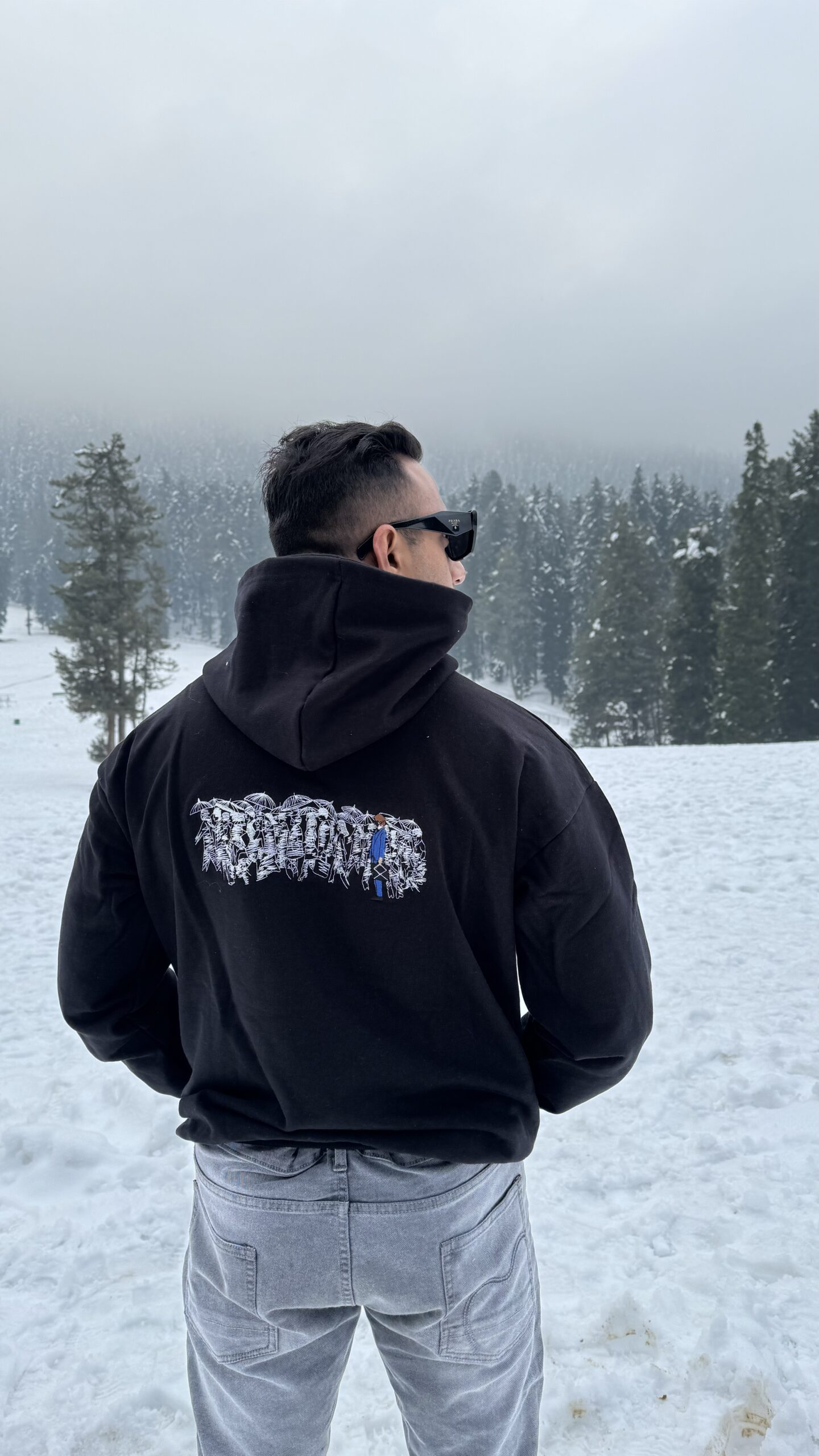 Person in a Karoshi embroidered hoodie amidst snowfall.